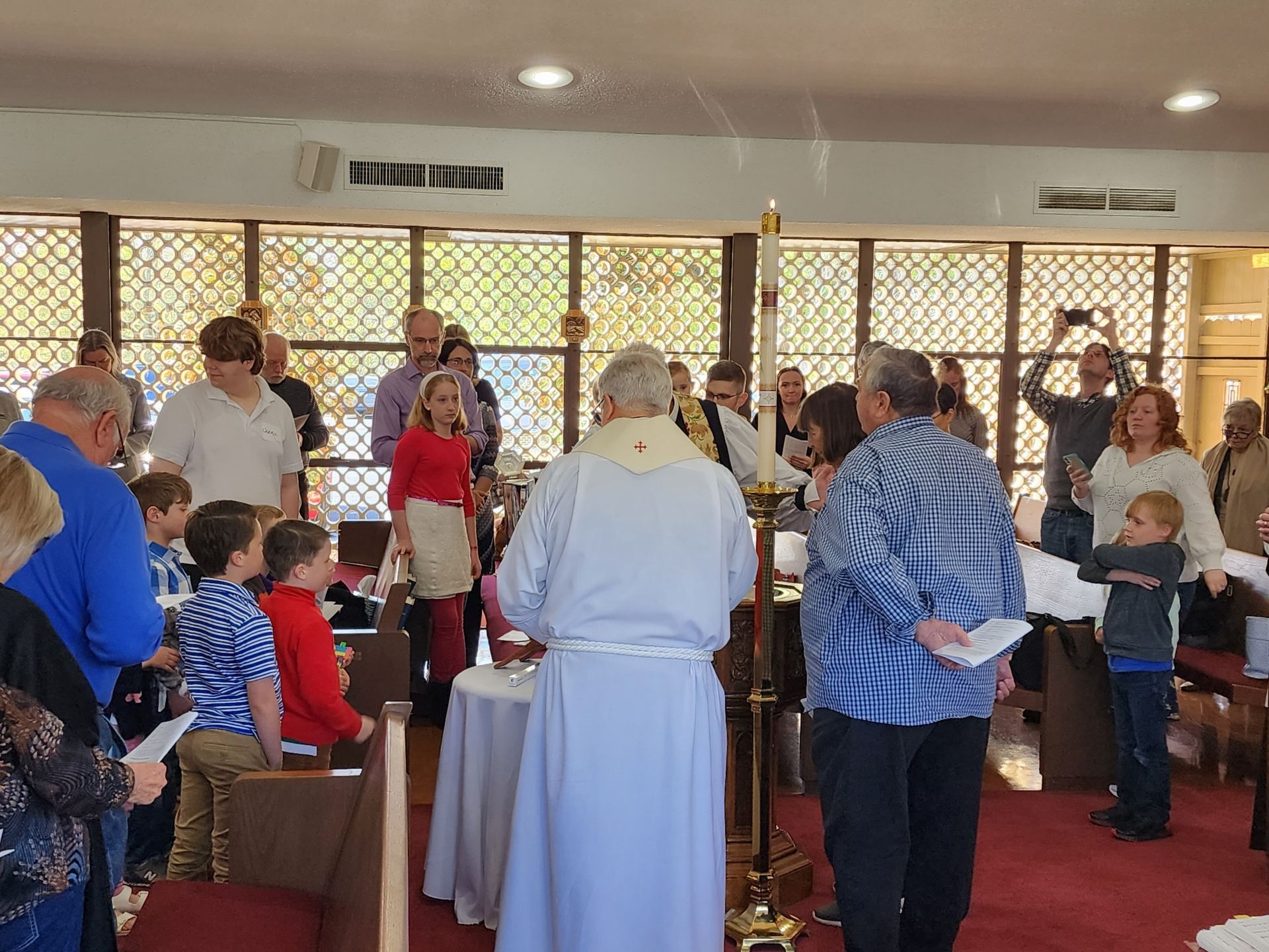 A priest stands at an altar, conducting a ceremony with a group of people inside a church.