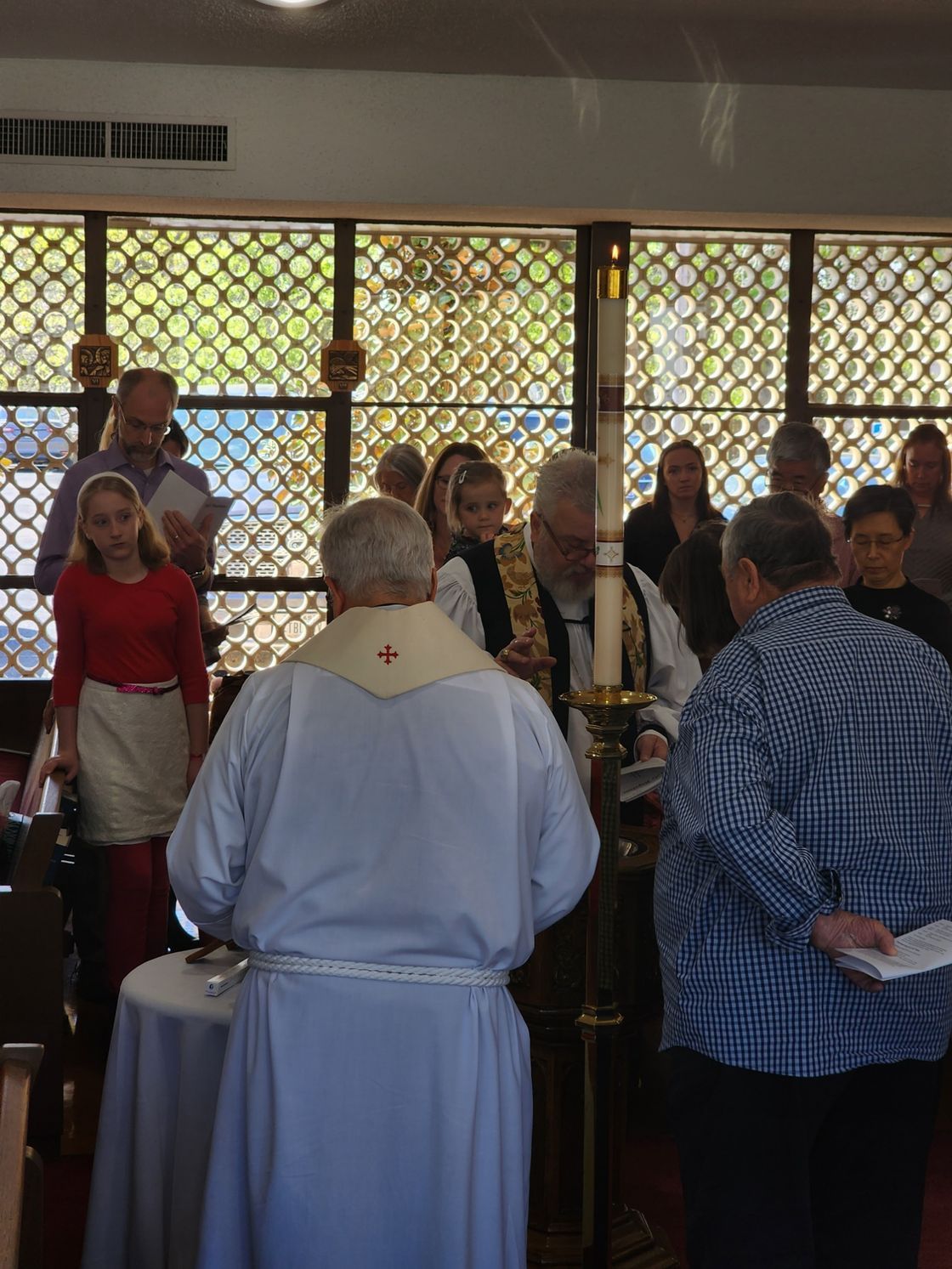 Clergy at a church ceremony, possibly baptism. People in attendance, stained glass window background.