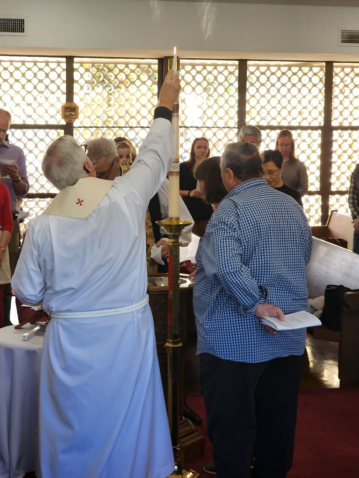 A priest holding a lit candle above a couple, performing a ceremony in a church.