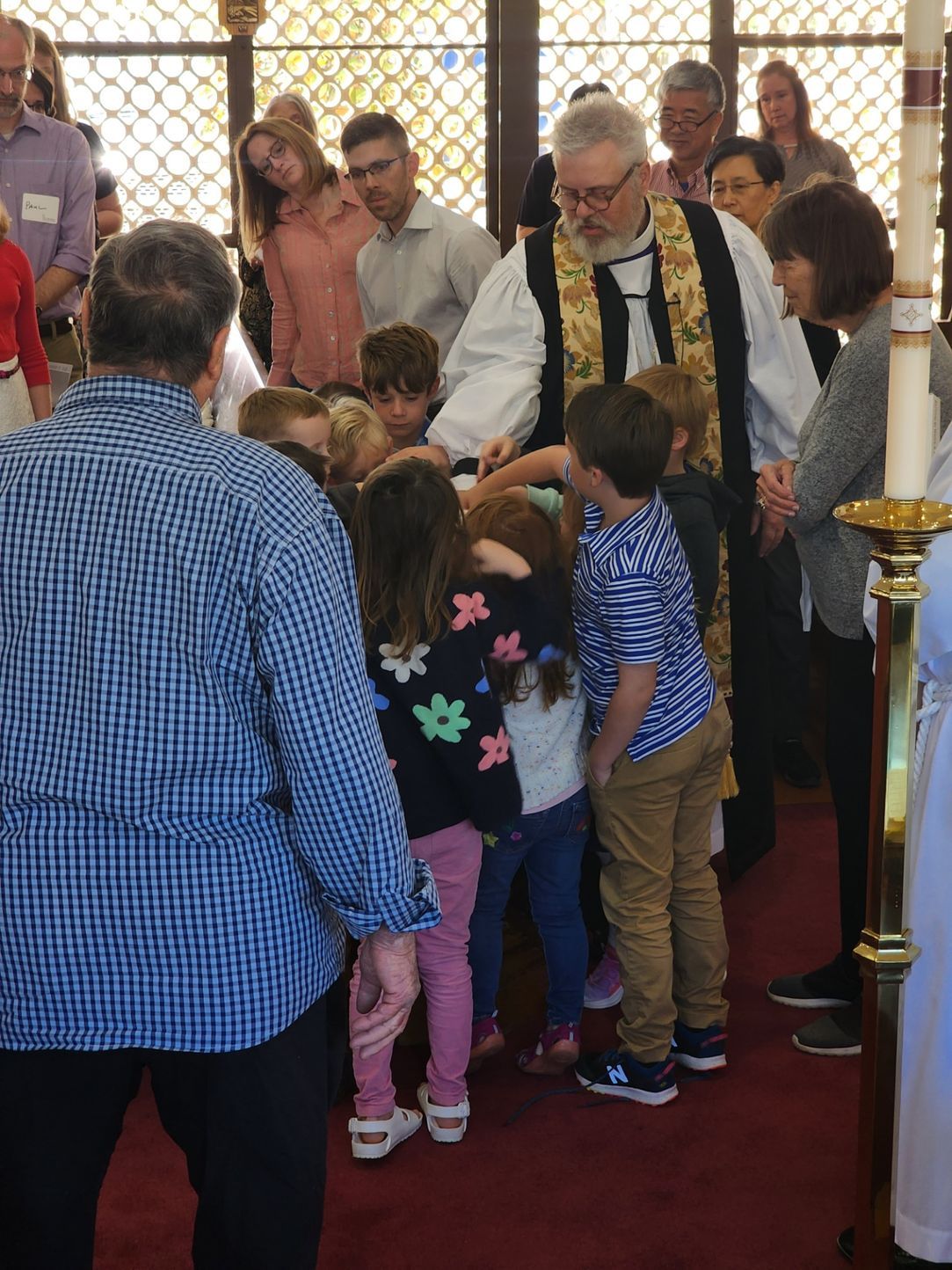 A priest blessing a group of children in a church; others watch.