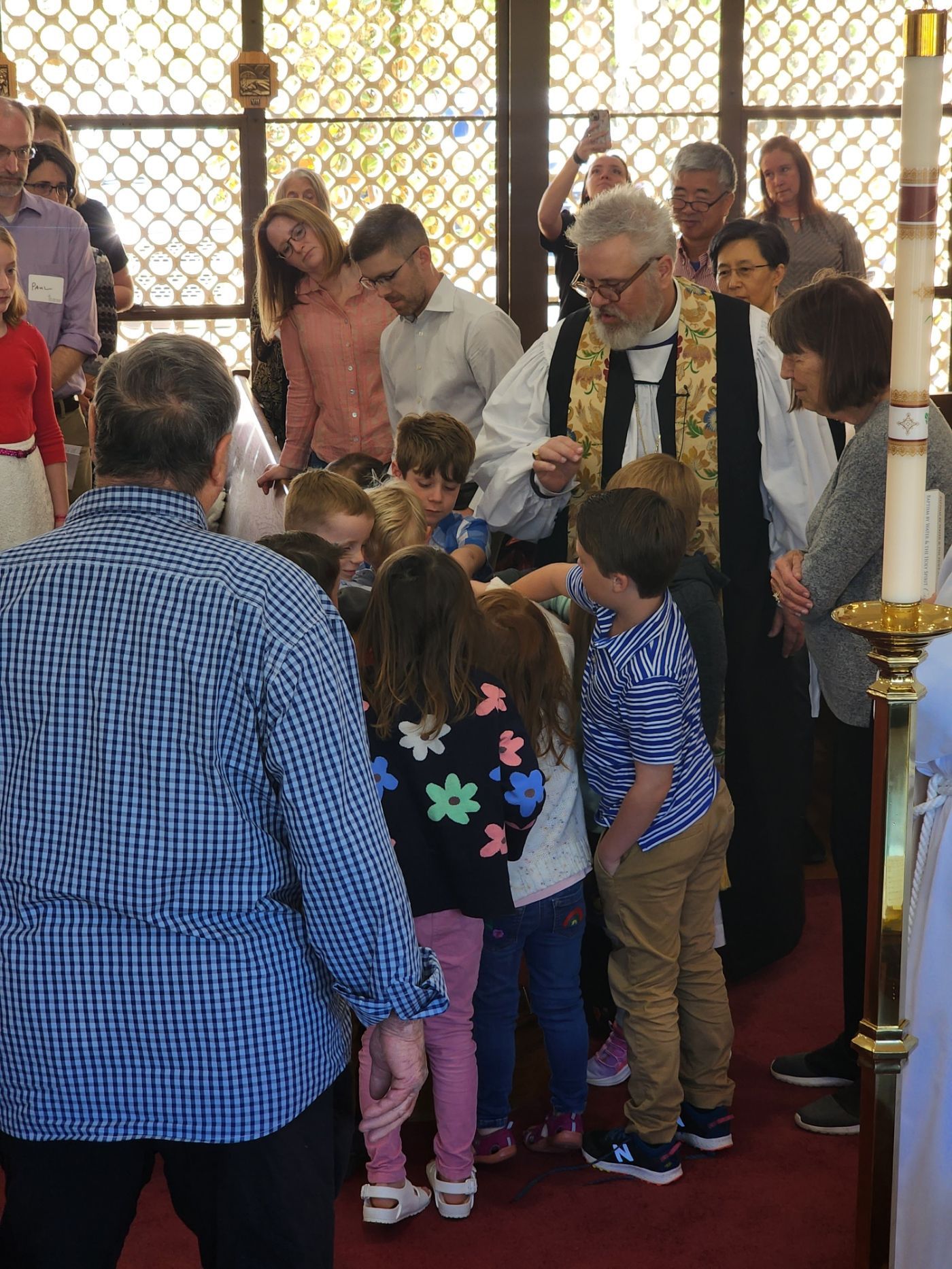 A priest administering communion to a group of children in a church. People watch nearby.