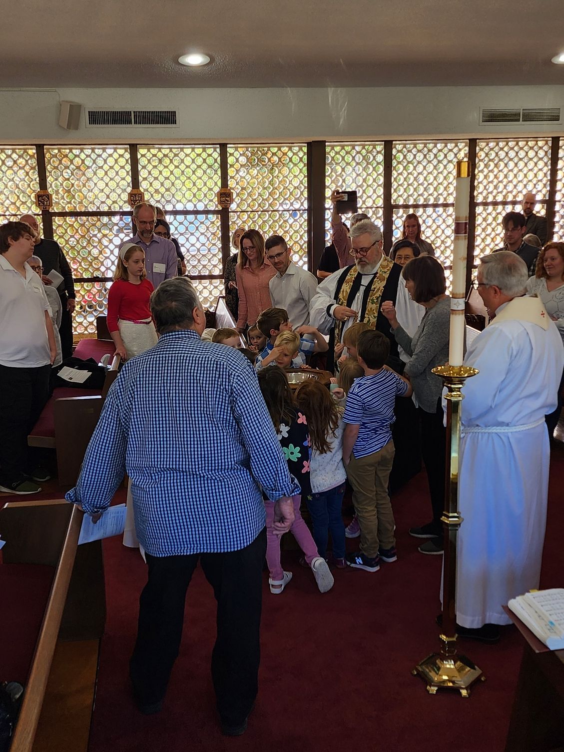 People gathered inside a church. A priest in white robes stands near a group of children, and adults look on.