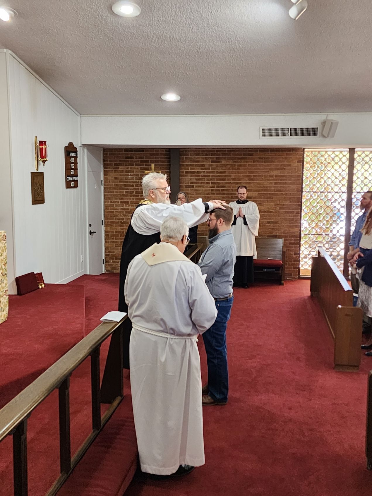 Clergy performing a religious ceremony, laying hands on a man in a church.