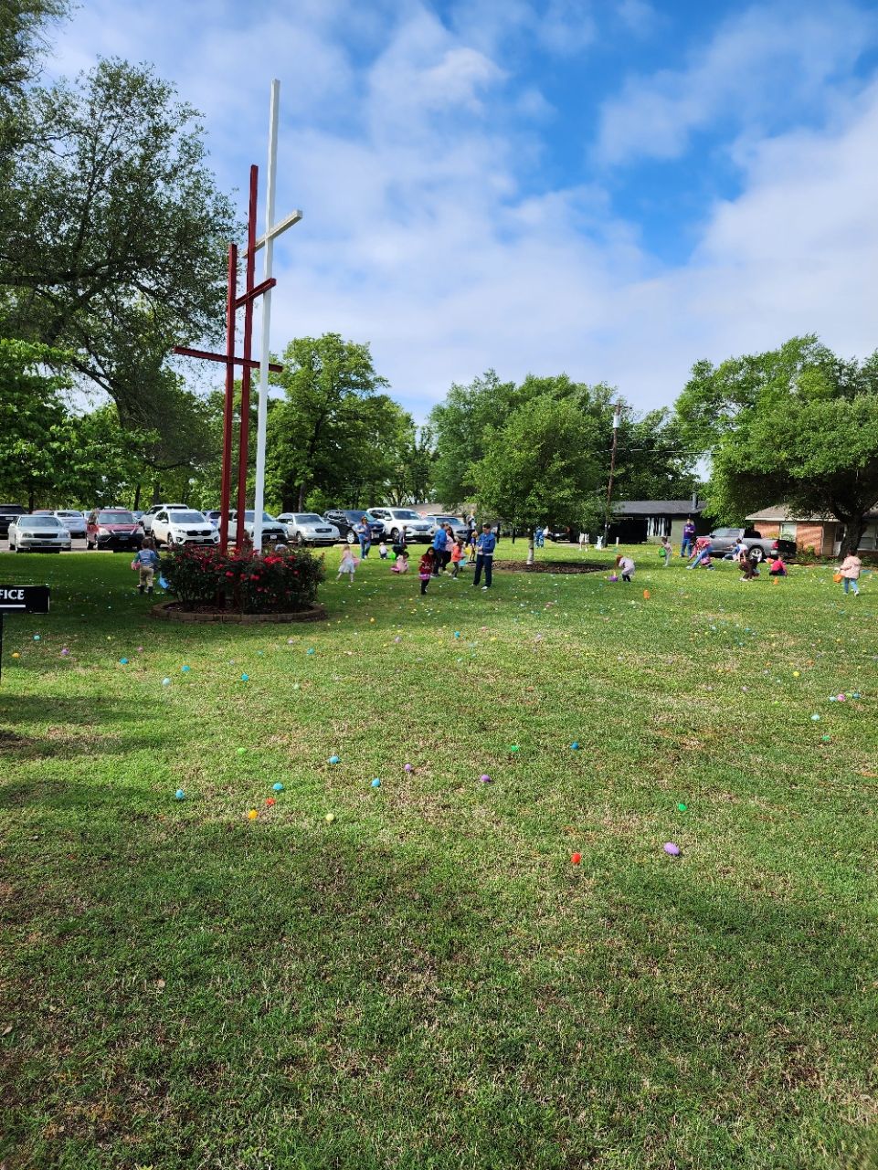 Children hunting for Easter eggs in a grassy field, with a tall wooden structure and a partly cloudy sky.