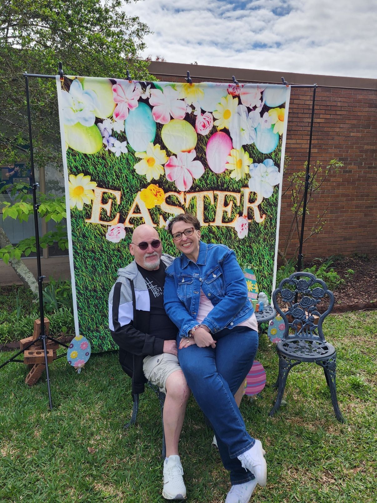 Couple sitting in front of Easter backdrop with eggs and flowers.