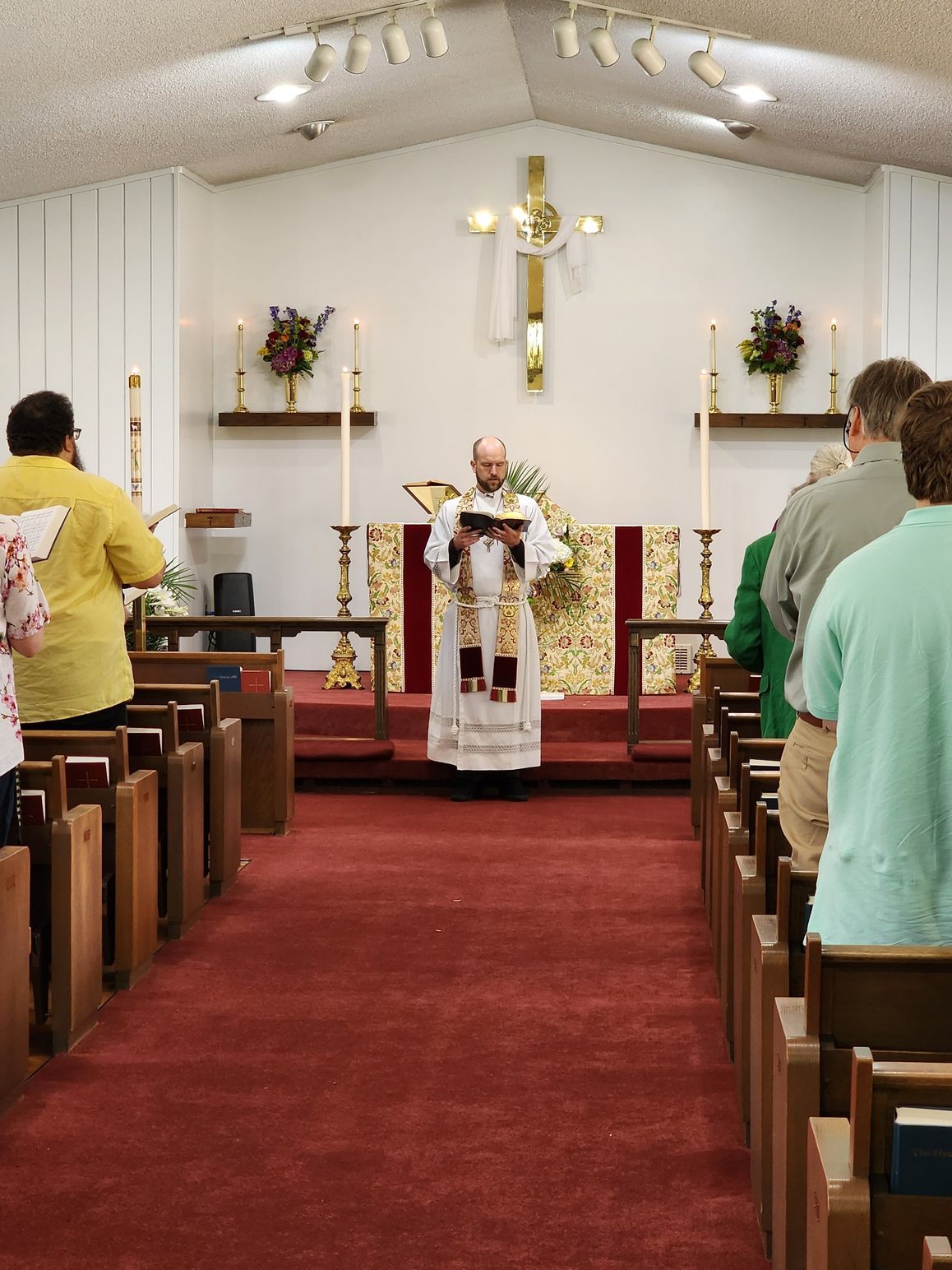A priest reads from a book at the altar of a church during a service.