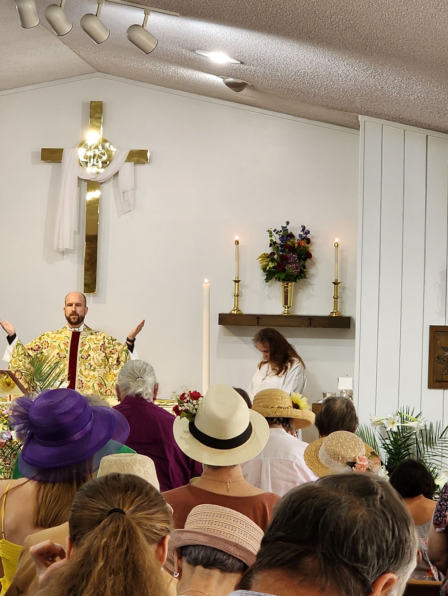 A priest leading a service in a church, with congregants wearing hats.