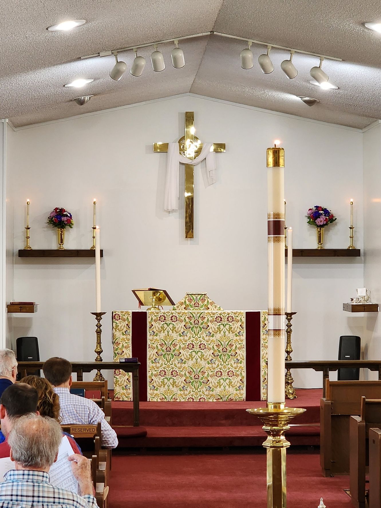 Church altar with cross, candles, and people in pews, likely a service.