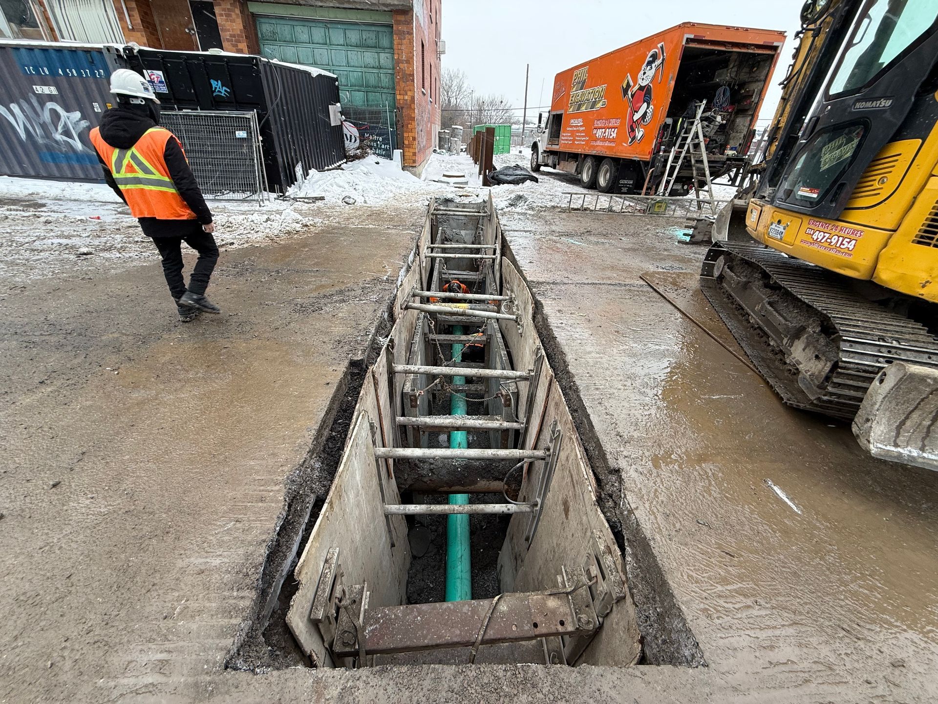 Construction site: Workers in orange vests beside a trench, equipment, and a red truck on a city street.