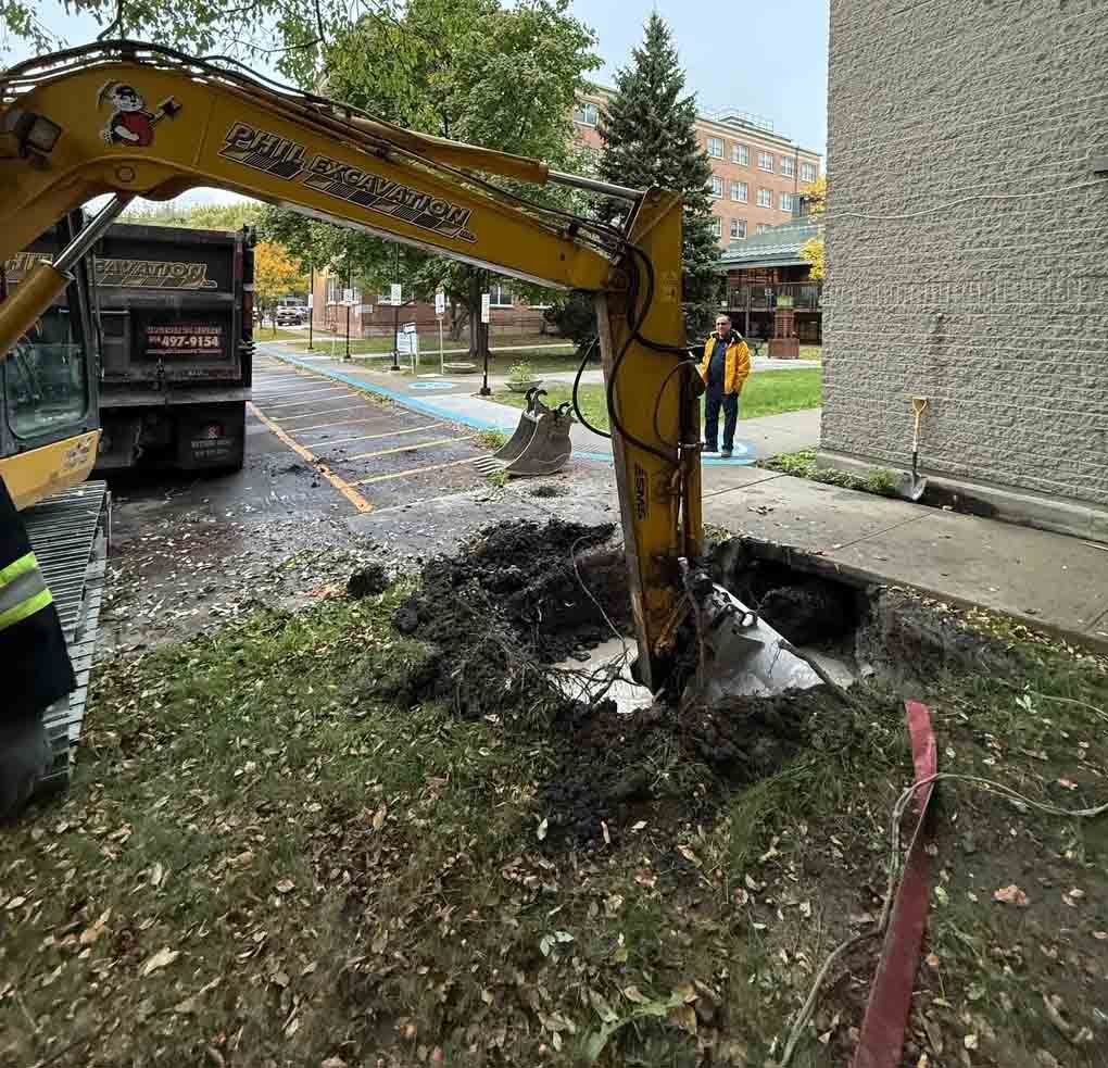 Chantier de construction avec tranchée ouverte, étaiement, excavatrice, camion et ouvriers.