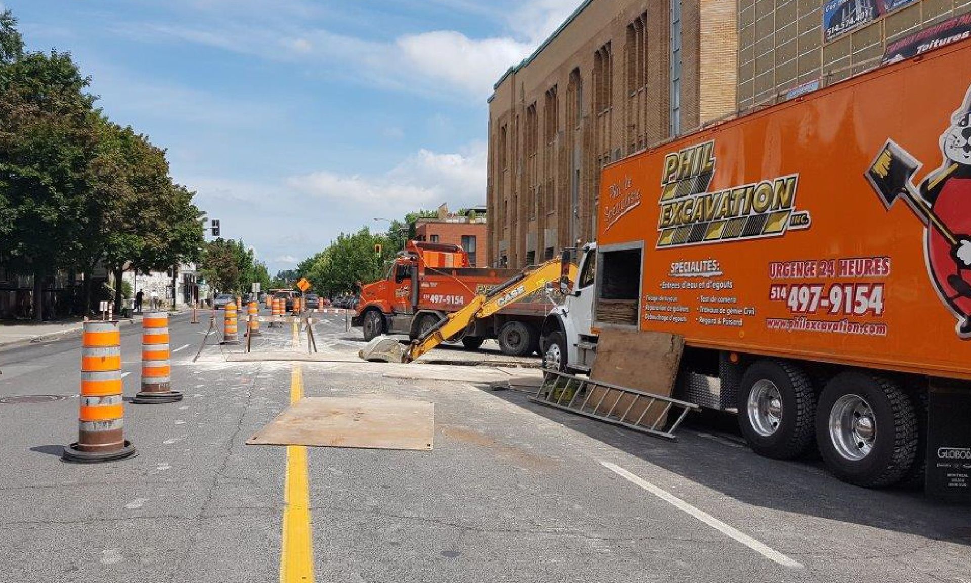 Travaux de voirie : camions orange, cônes de signalisation, débris, excavatrice, bâtiment.