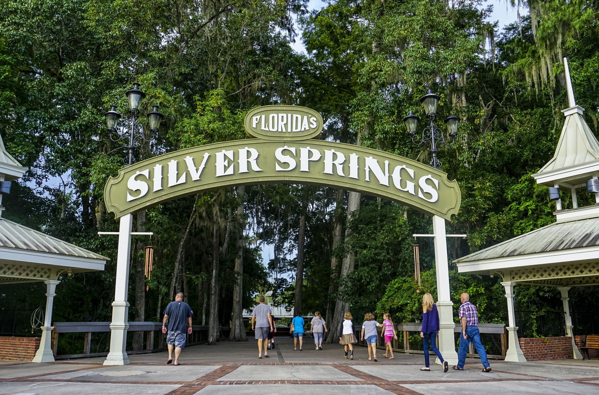 Visitors walk through an ornate green entrance archway reading