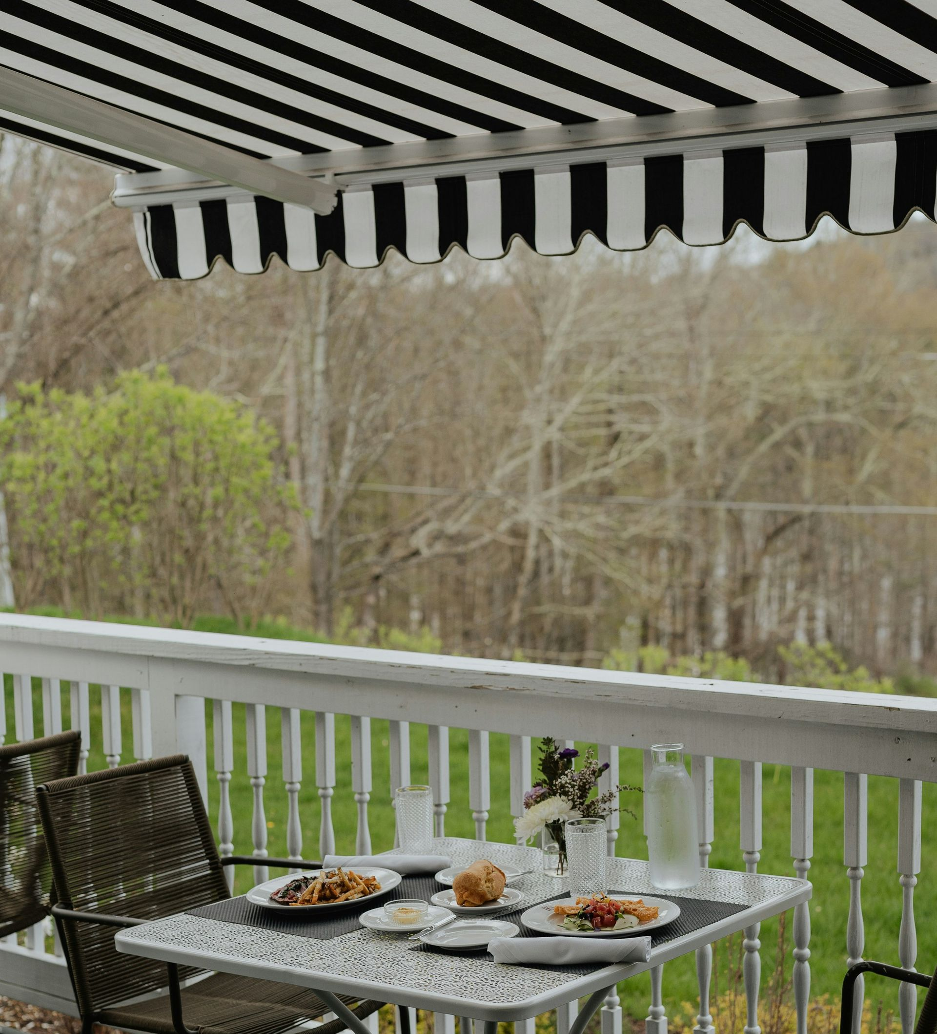 Patio table with food under a black-and-white striped awning overlooking a wooded yard