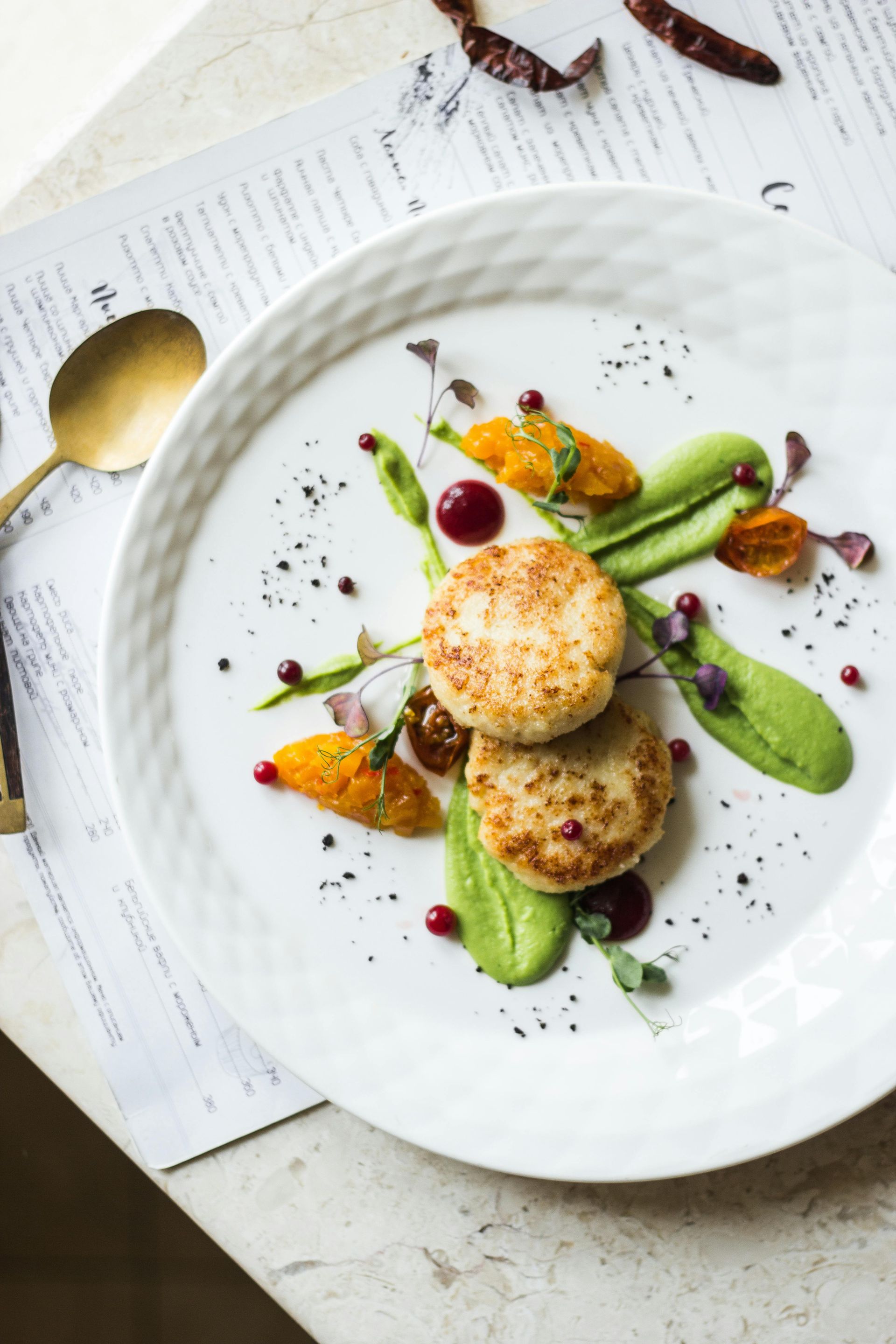 Two seared patties, green puree, orange puree, and red berries on a white plate.