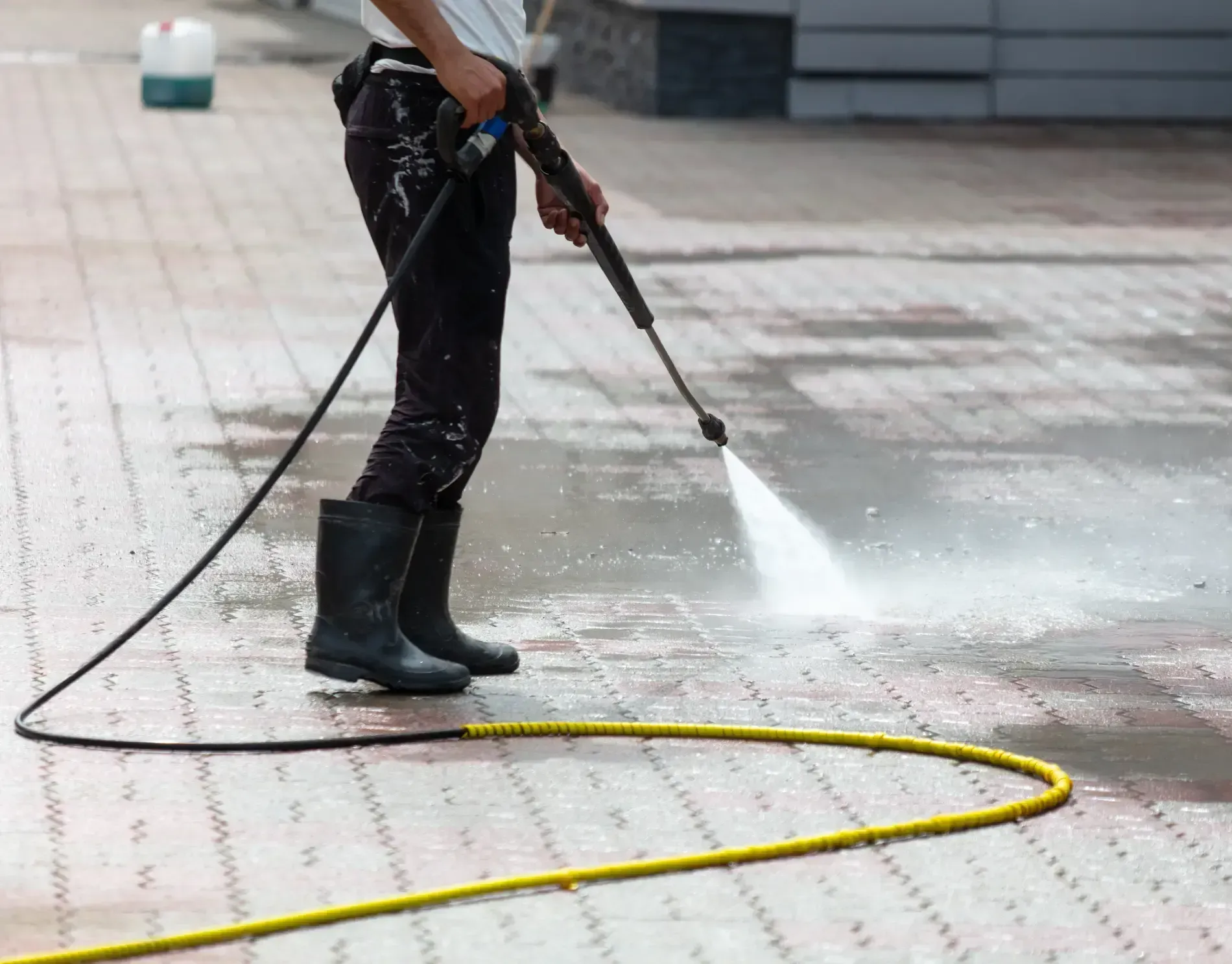 Person power washing a brick paved surface with a pressure washer, wearing black boots.