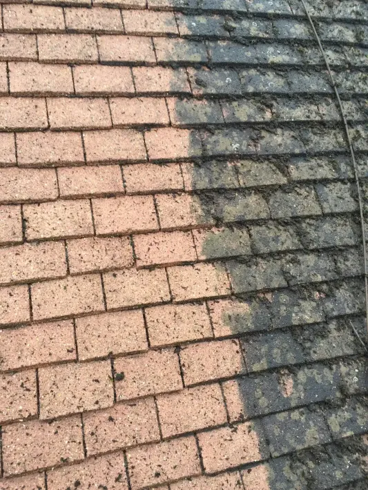 A split view of a roof showing a cleaned, light-colored side next to a dirty, dark side covered in algae and debris.