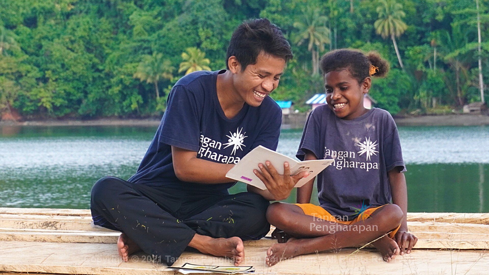 A man and a girl are sitting on a dock reading a book.