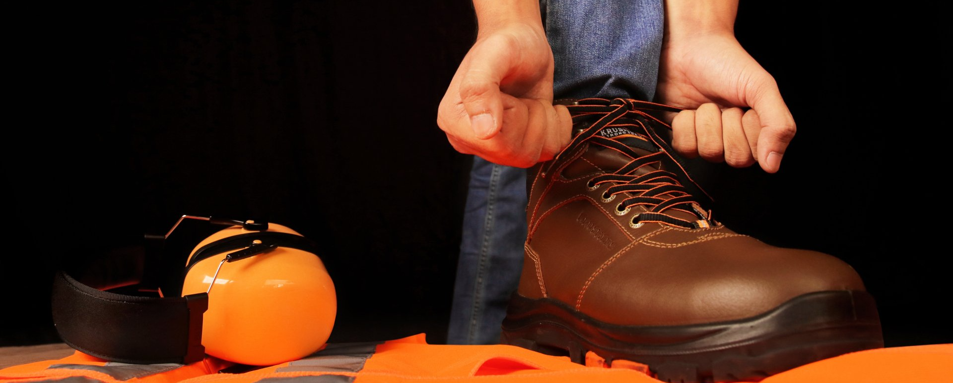 A person is tying a pair of boots next to a pumpkin.