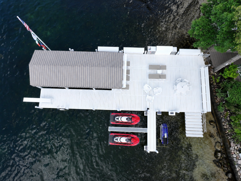 Two workers in waders and high-visibility shirts install a white wooden pier in a lake using a barge-mounted crane.