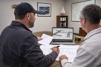Two people review architectural plans and a 3D digital model of a dock in an office.