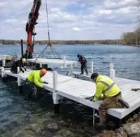 Construction crew using a crane-equipped barge to install a white modular dock into a lake.