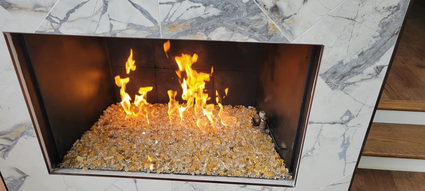 A fireplace with yellow flames burning atop a bed of tan rocks, set in a marble surround.
