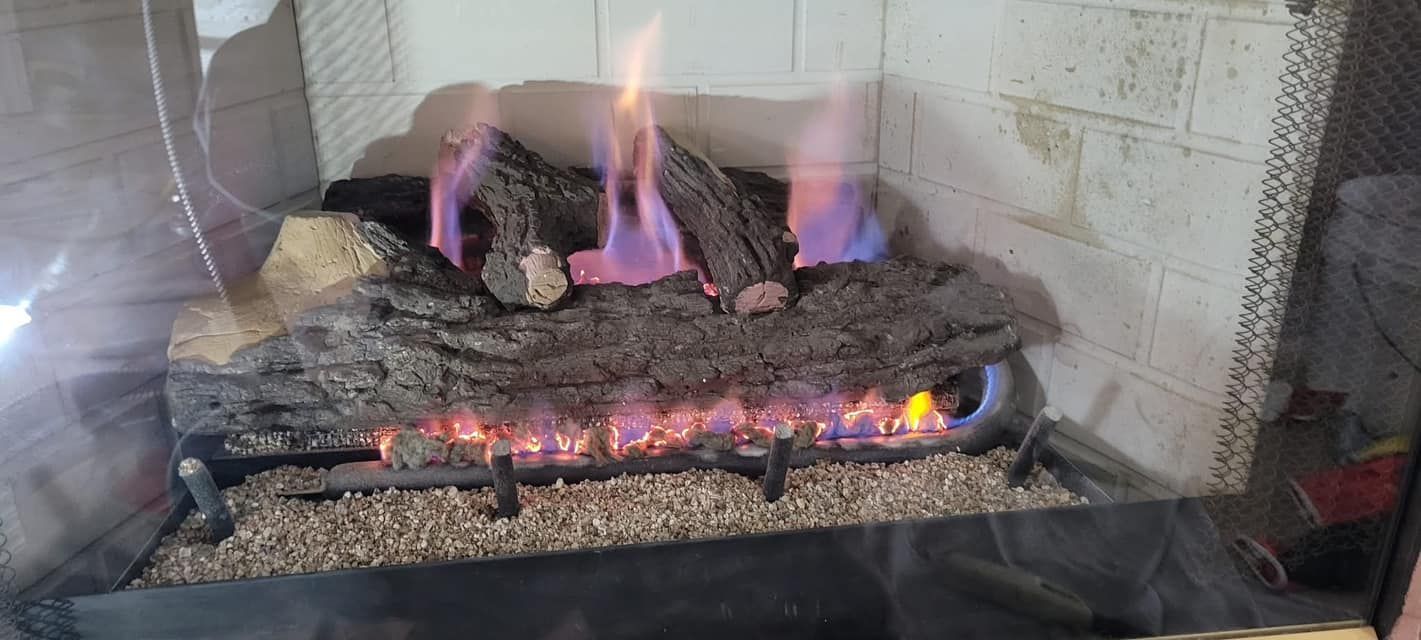 A gas fireplace with flames emitting from artificial logs, set in a stone hearth.