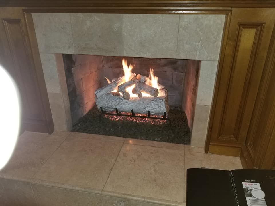 Fireplace with burning gas logs, framed by light-colored stone and wood.