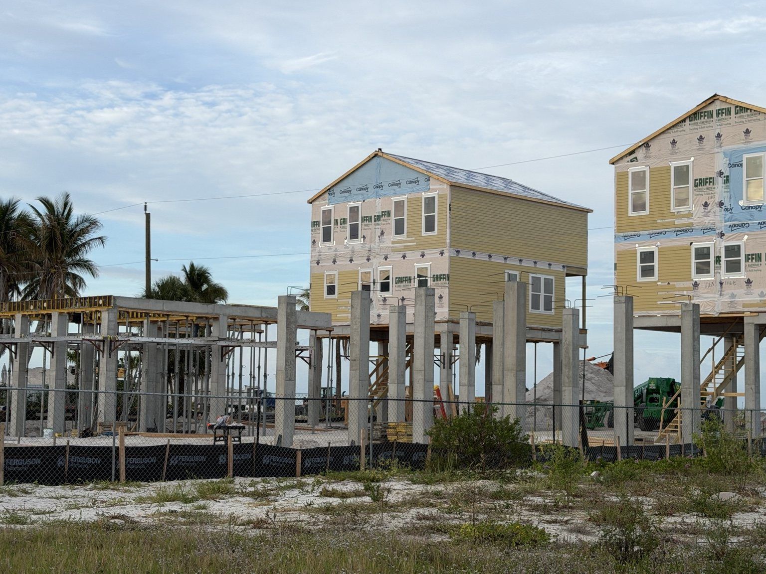 Partially built coastal houses with exposed framing under a cloudy sky