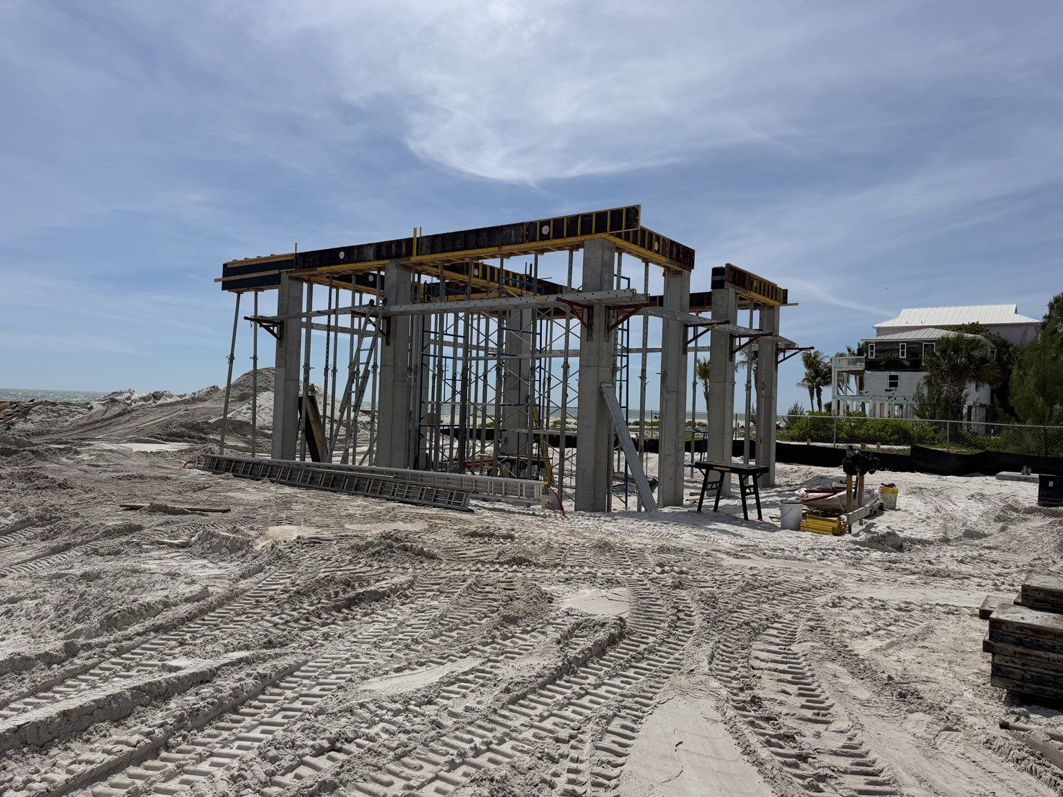 Partially built concrete structure on a sandy construction site under a cloudy sky