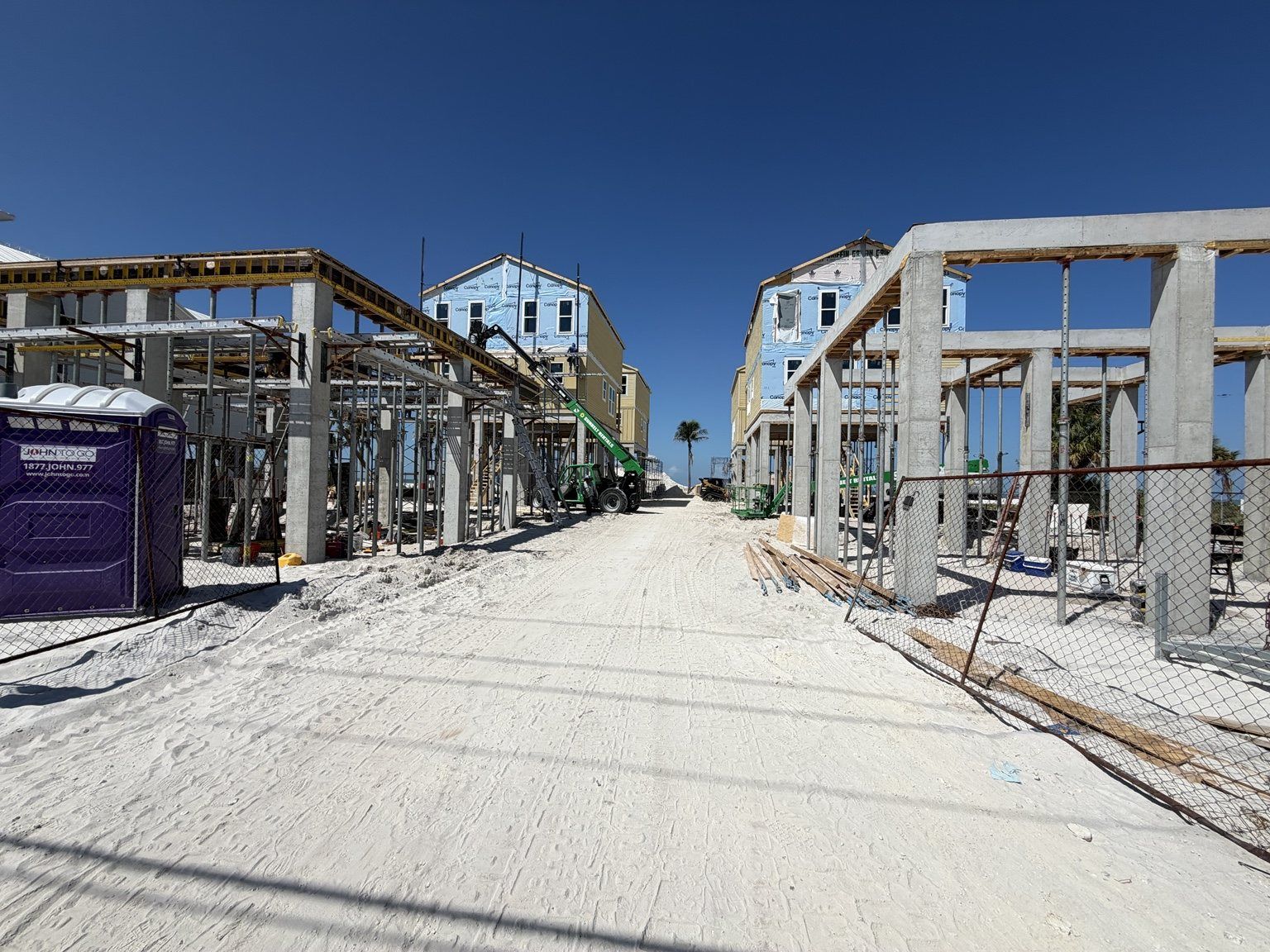 Partially built houses lining a wide sandy street under a clear blue sky