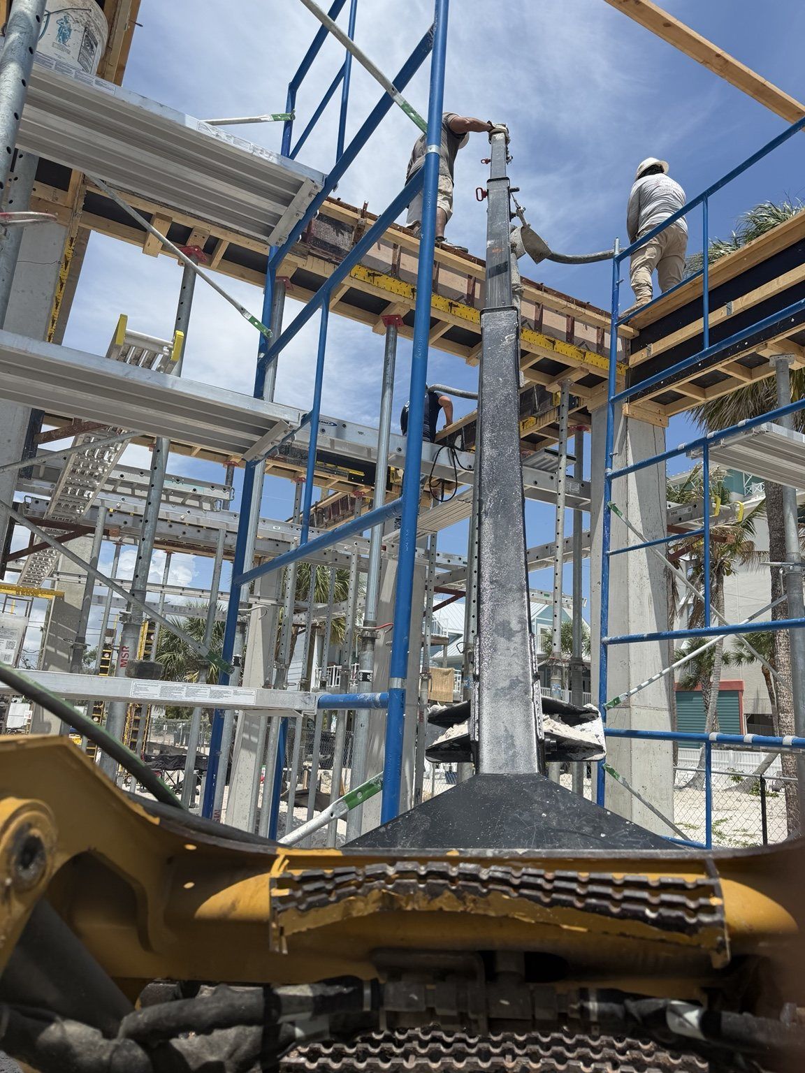 Construction site with workers on scaffolding and a yellow excavator arm in the foreground