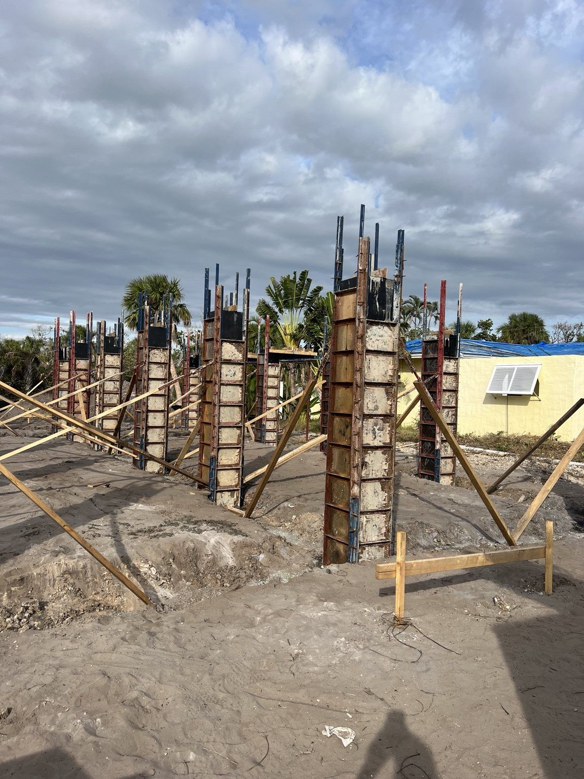 Concrete foundation columns with wooden formwork and supports at a construction site under cloudy skies