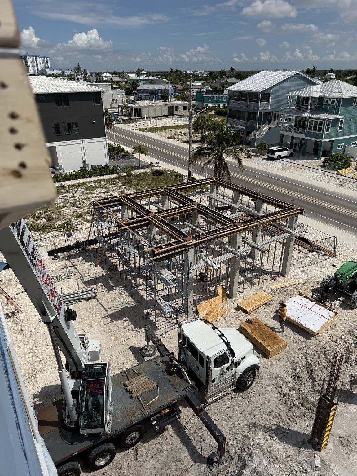 Construction site with steel frame and trucks in a coastal neighborhood.