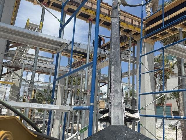 Blue steel framework at a construction site with yellow walkways and palm trees in the background