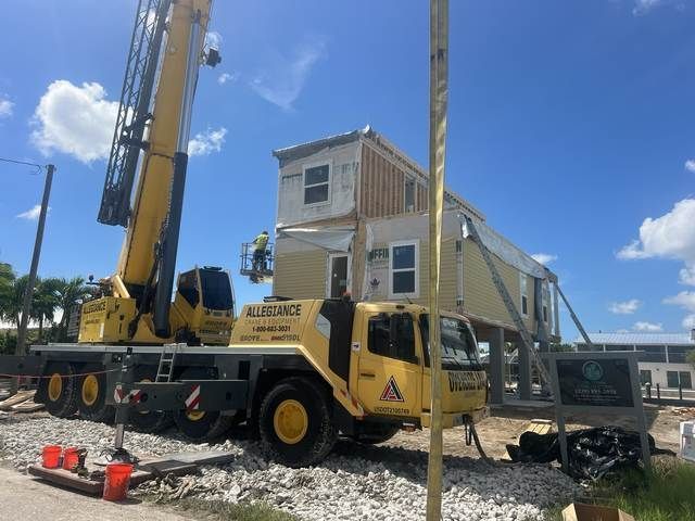Yellow crane lifting a two-story house module on a construction site under a blue sky