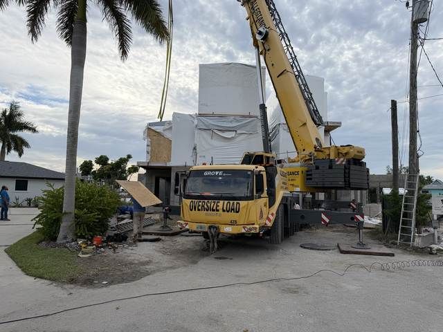 Yellow crane truck lifting debris beside a damaged white building on a roadside