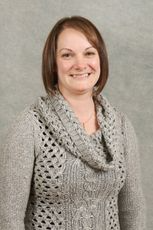 Woman wearing a gray sweater, smiling in a studio setting.