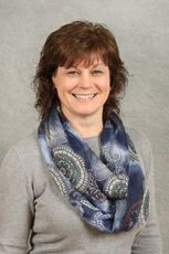 Woman wearing a gray sweater and blue paisley scarf smiles at the camera.