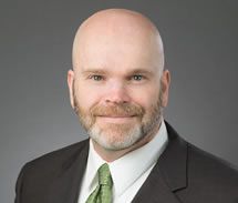 Bald man with beard in suit and tie, smiling, studio shot.