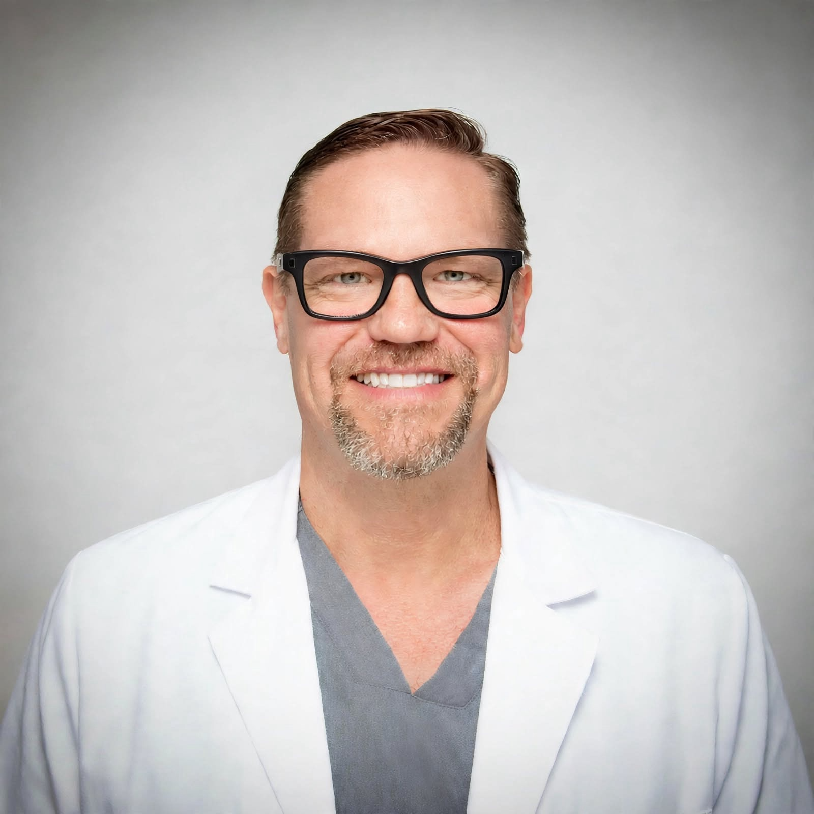 Smiling man with a goatee, wearing a blue polo shirt, in front of a patterned background.