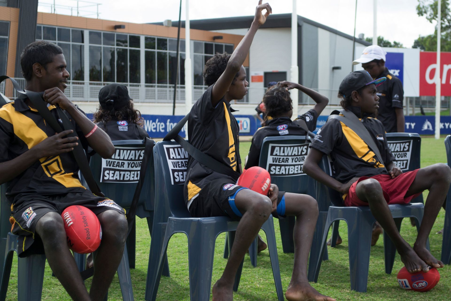 A group of people are sitting in chairs on a field and one of them is raising his hand.