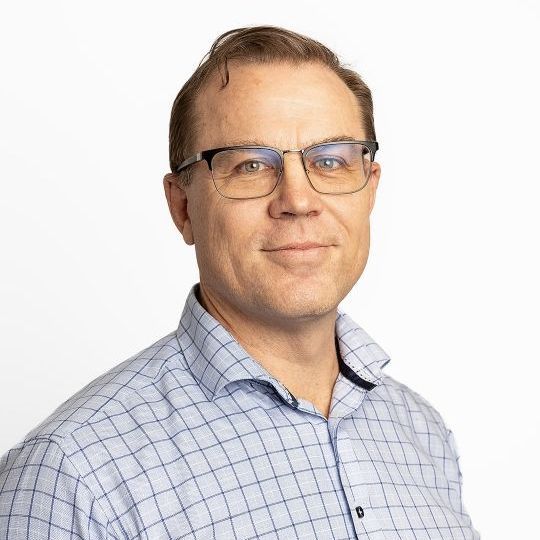 A man wearing glasses and a blue shirt is smiling for the camera.