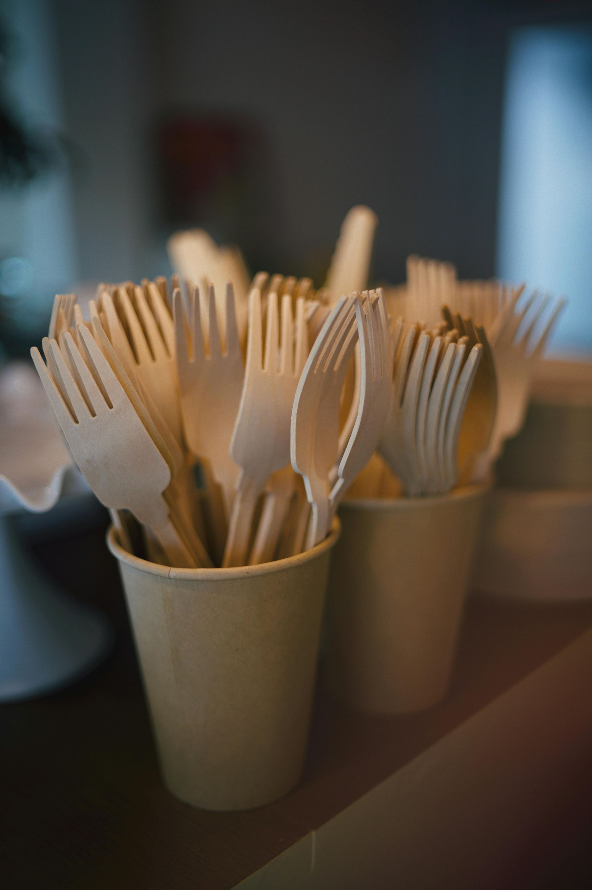 Paper cups filled with wooden forks and spoons on a table, softly lit indoors