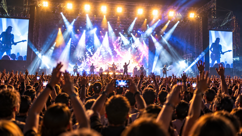 Pubblico che esulta durante un concerto dal vivo con luci di scena brillanti e artisti sul palco.