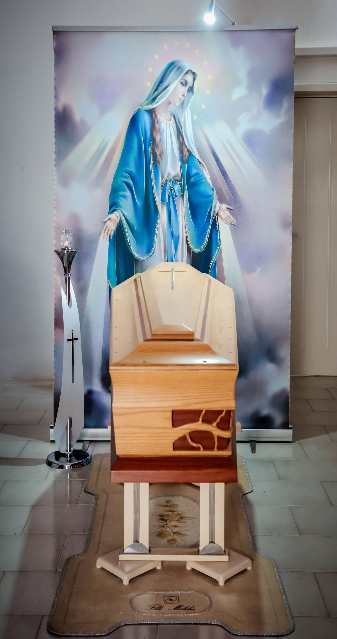 Una bara di legno è posta davanti a un'immagine della vergine Maria.