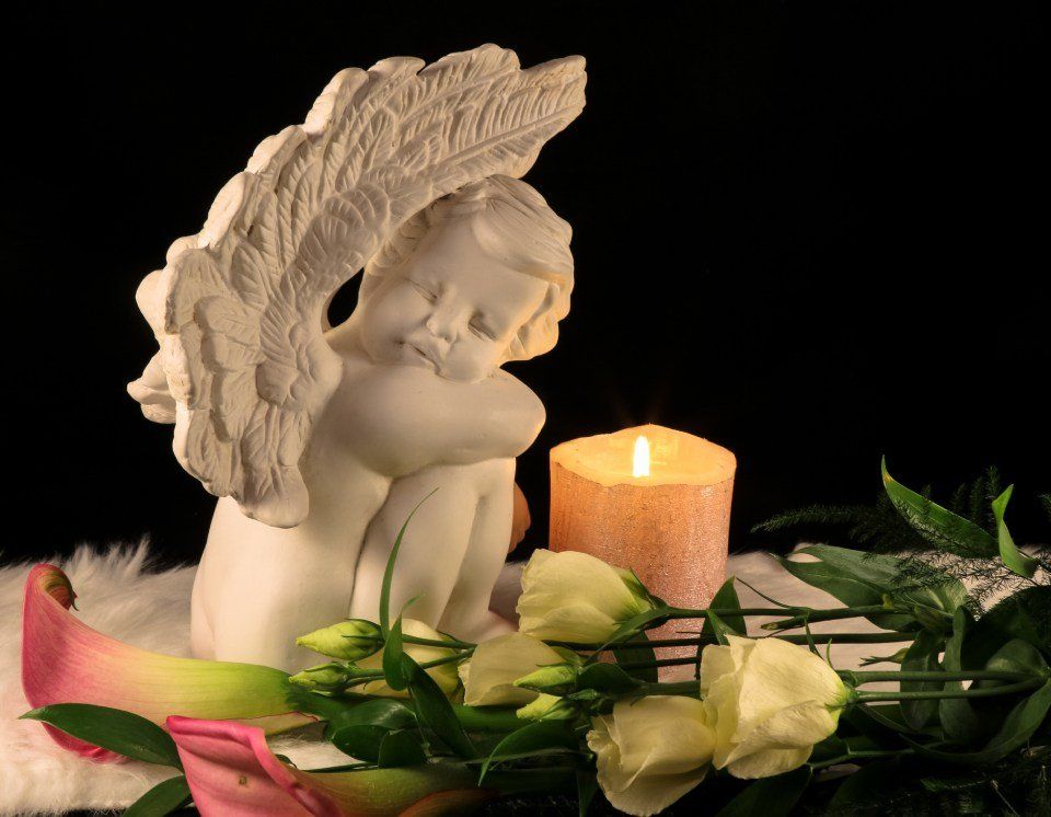 Una statua di un angelo è seduta accanto a una candela e dei fiori.