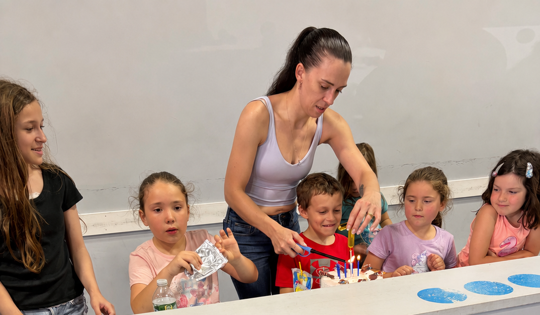 Teacher helping children with a craft activity at a table, with colorful supplies and drawings.