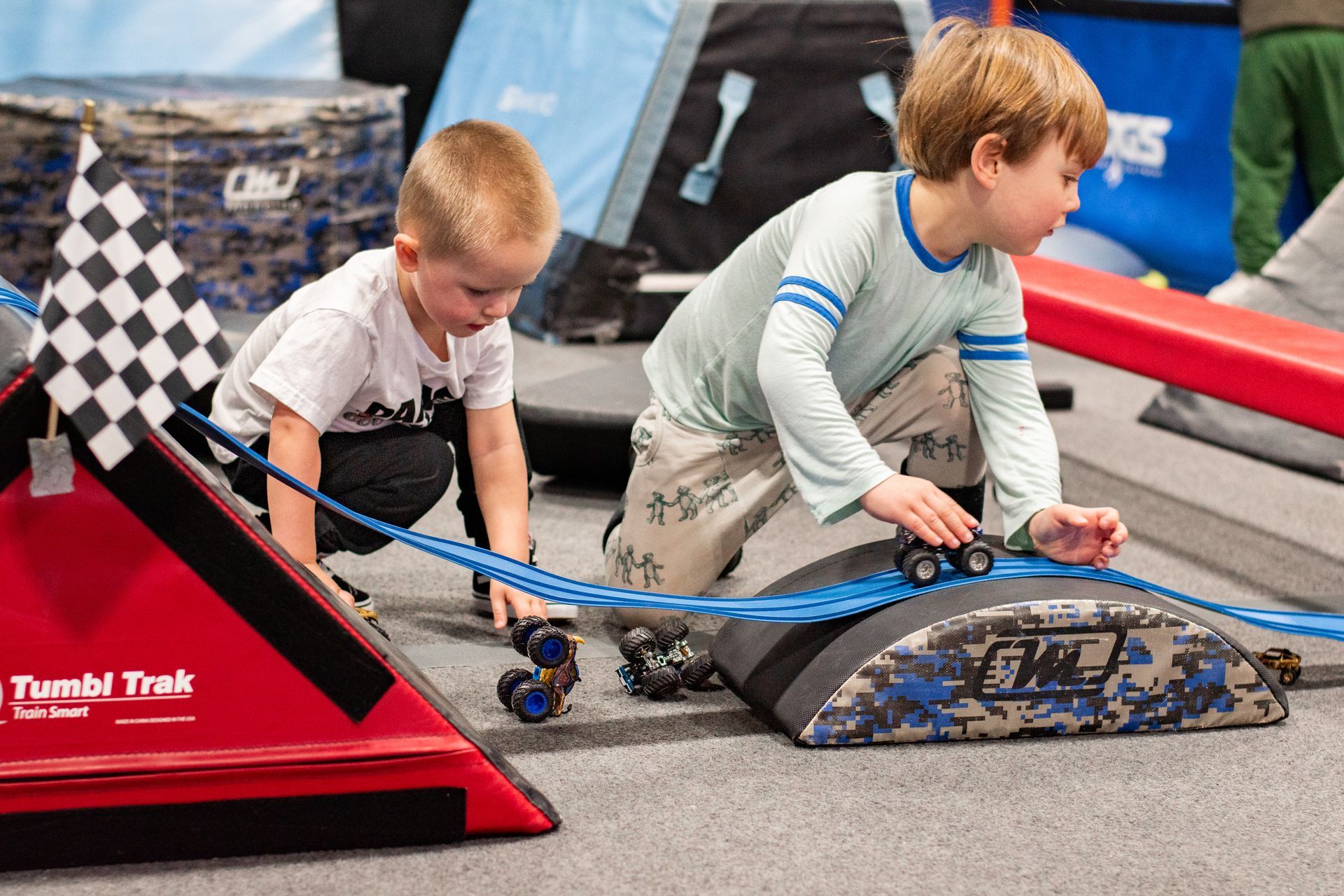 Two children racing small vehicles on a track, one crossing a checkered finish line