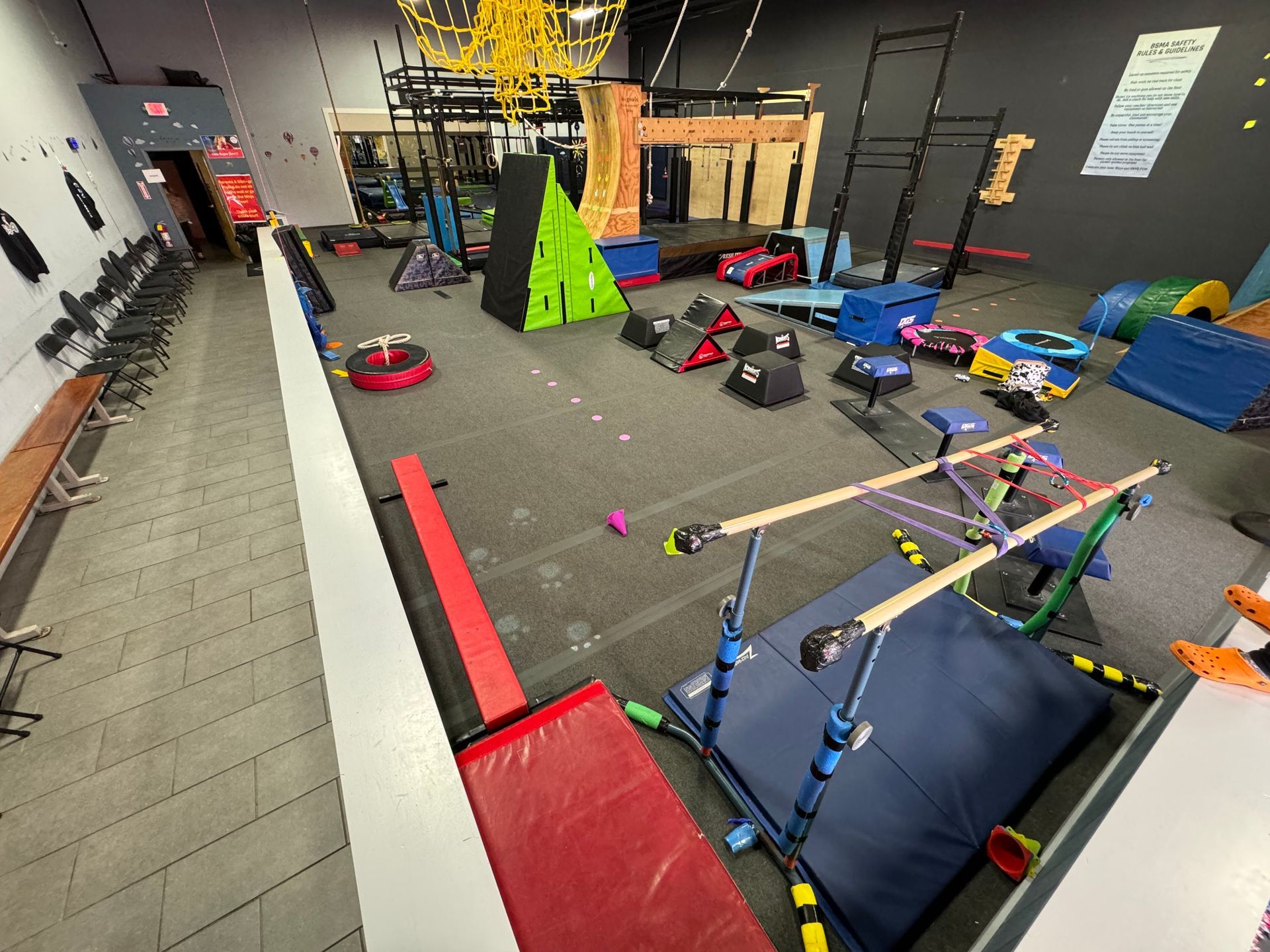Indoor play room with foam obstacles, scooters, balance beams, and climbing structures on a black floor